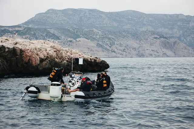 Divers in full gear aboard a small dive boat next to a rocky coast
